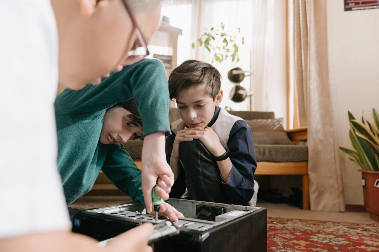 Three children collaborating to repair a computer, using tools indoors.